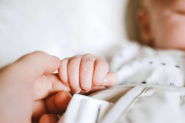 A person's hand gently holding the tiny hand of a baby. The person's fingers wrap around the baby's hand, demonstrating a gesture of tenderness and protection. The baby's fingers are small and delicate, illustrating their fragility and innocence.